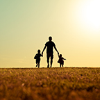 father holding the hands of children at sunset
